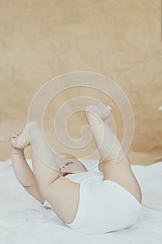 6-8-month-old baby boy lying playfully in bed. Charming 6-7 month little baby in white bodysuit. Baby boy in white bedding. Copy