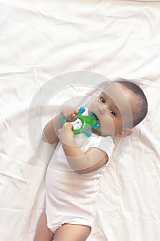 6-8-month-old baby boy lying playfully in bed. Charming 6-7 month little baby in white bodysuit. Baby boy in white bedding. Copy