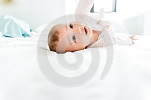 6 month old baby looking at camera in the morning lying on the bed between white sheets