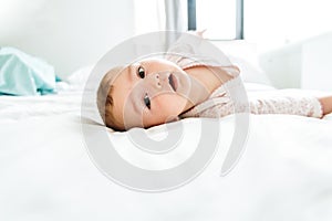 6 month old baby looking at camera in the morning lying on the bed between white sheets