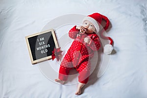 6 Six months old baby laying down on white background wearing Santa costume. Flat lay composition.