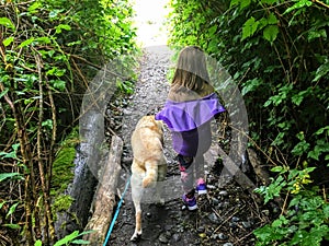 A 6 year old girl walking along a trail with her dog outside Sooke, surrounded by forest. On Vancouver Island, British Columbia