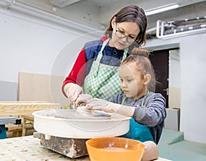 6 years old girl sculpts from clay under the guidance of a mature woman.