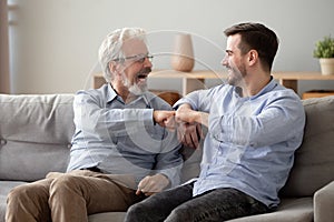 60s man and millennial guy giving fist bump sitting indoors