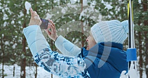 A 65s adult female skier in a blue ski suit in a winter forest takes photos