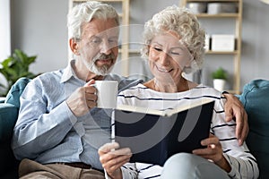 65s spouses resting at home reading book drinking beverage
