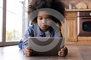 6s African girl lying on warm kitchen floor with tablet