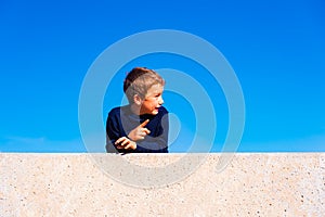 A 7 year old boy isolated on blue sky background points his finger with funny expression