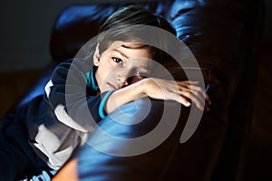 7 year old Caucasian boy is bored without friends, lying on sofa in his room.