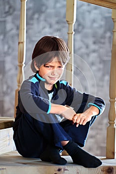 7 year old European boy frowned while sitting on stairs at home.
