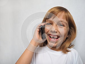 7-year-old girl with no front tooth. The child is talking on the phone or smartphone and laughs cheerfully. Change of milk teeth