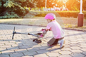 A 7-year-old girl in a pink helmet and protective gear fell off a scooter. The concept of safe riding a scooter and a