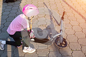 A 7-year-old girl in a pink helmet and protective gear fell off a scooter. The concept of safe riding a scooter and a