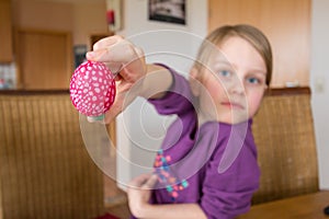 A 7 year old girl smiles and holds an easter egg into the camera, depth of field