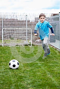 7 years boy kicking ball in the garden.