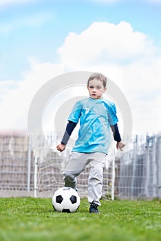 7 years boy kicking ball in the garden.