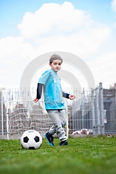 7 years boy kicking ball in the garden.