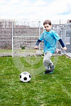 7 years boy kicking ball in the garden.