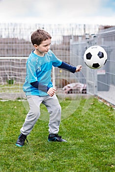 7 years boy kicking ball in the garden.