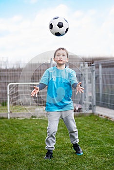 7 years boy kicking ball in the garden.