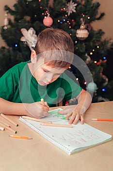 7 years old boy write letter to Santa sitting by desk