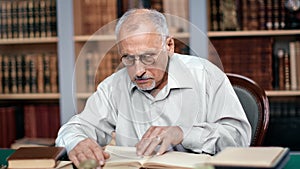 70s grandfather teacher professor scientist reading ancient paper book sitting at public library