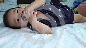8 Month old Asian Chinese baby boy lying on bed with playing his pacifier