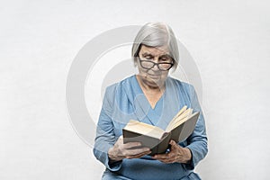 80s woman with gray hair and wrinkled skin reads a book.