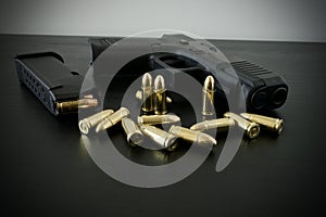 9 mm handgun with fully loaded magazine and bunch of golden brass ammo spilled on black wooden desk