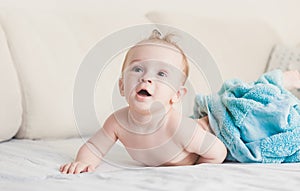 9 months baby boy under blue towel on bed with white sheets