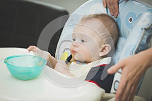 9 months old baby boy sitting in highchair and reaching for dish