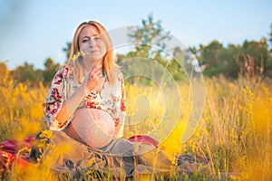 9 months pregnant woman sitting in yellow grass and smiling. Waiting for baby. Pregnancy concept.