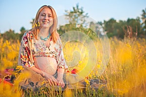 9 months pregnant woman sitting in yellow grass and smiling. Waiting for baby. Pregnancy concept.
