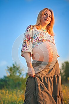 9 months pregnant woman sitting in yellow grass and smiling. Waiting for baby. Pregnancy concept.