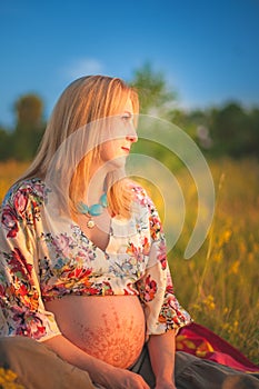 9 months pregnant woman sitting in yellow grass and smiling. Waiting for baby. Pregnancy concept.