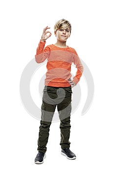 A 9-year-old boy in jeans and an orange sweater stands and shows the ok sign. Isolated on white background. Vertical