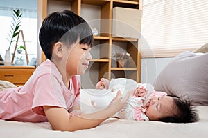 A 9-year-old boy is playing in bed with his 3-month-old newborn sister. An Asian boy is taking care of his sister in bed while