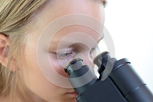 A 9 year old girl looks into the eyepiece of a microscope.