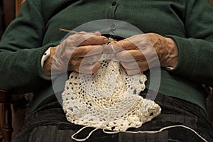 A 90-year-old lady crochets with white yarn