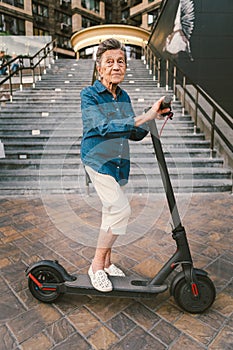 90 year old woman with gray hair, wrinkles, progressive and active uses modern electric transport scooter. Lady