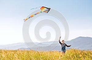 9YO Smiling girl with flying colorful kite running on the high grass meadow in the mountain fields. Happy childhood moments or