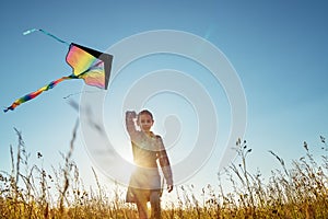 9YO Smiling girl with flying colorful kite running on the high grass meadow in the mountain fields and smiling at the camera.
