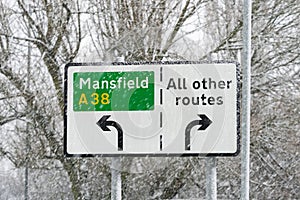 A38 road sign to town and motorway snowing during winter. Settled snow on directional sign with all other routes arrows left right