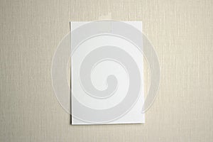 A4 white sheet of paper hanging on a wall glued with a piece of paper tape on a light background