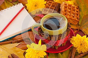 Aa cup of coffee, a notebook, homemade waffles, maple leaves, autumn flowers and cinnamon sticks