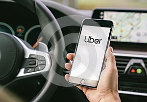 Uber driver holding smartphone in car. Uber is an American company offering different transportation services online