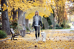 Aattractive young woman walking with her lovely golden retriever dog in the park in autumn