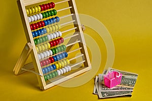 Abacus and shopping basket with dollars at yellow background. Shopping, personal finances, money spendings concept