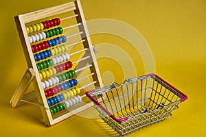 Abacus and shopping basket at yellow background. Shopping, personal finances, money spendings concept