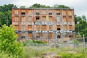 An abandoned and boarded up older building with graffiti and overgrown exterior